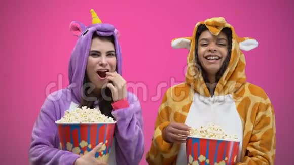 两个女人穿着独角兽和长颈鹿睡衣吃爆米花看喜剧视频的预览图
