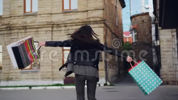 激动的年轻女子拿着纸袋在街上旋转用照相机看镜头的慢镜头肖像视频的预览图