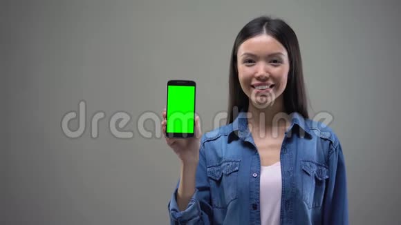 快乐的亚洲女人展示智能手机绿色屏幕网上银行购物视频的预览图