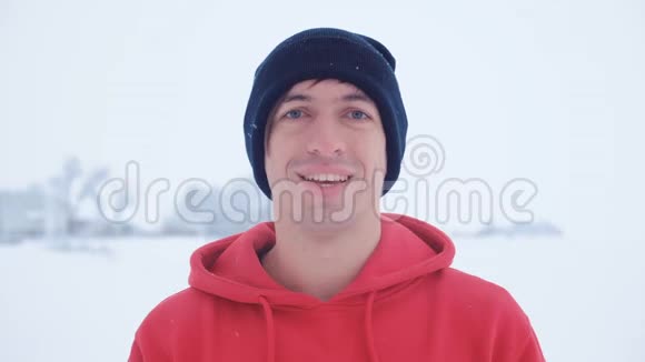黑帽年轻人的画像在冬季寒冷的户外雪地里微笑视频的预览图