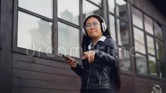 慢动作的快乐亚洲女孩听音乐戴无线耳机和跳舞移动的手和身体行走视频的预览图