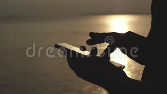 在海滩上的金色夕阳下男性手使用触摸电话慢动作1920x1080视频的预览图