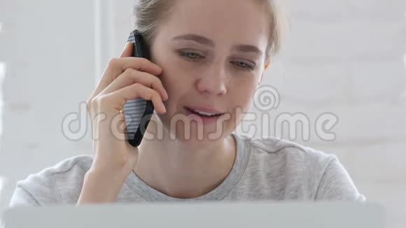 一位年轻女子一边打电话一边用笔记本电脑工作视频的预览图