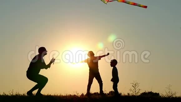 日落时幸福家庭的剪影爸爸和两个孩子在大自然中玩风筝视频的预览图