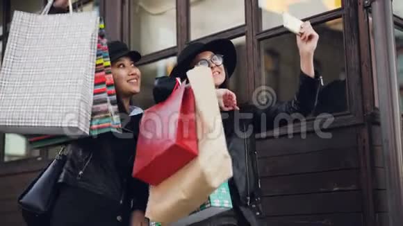 兴奋的女性朋友美丽的女孩在秋天拿着智能手机自拍拿着购物袋视频的预览图