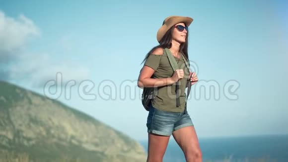 徒步旅行的女人戴着太阳镜和帽子享受着穿越大海和山脉的奇妙景观视频的预览图