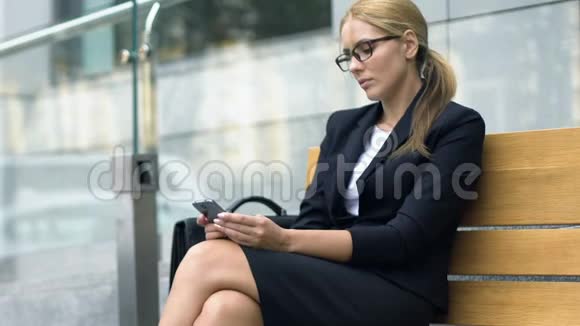 女士在智能手机上聊天坐在长凳上等出租车小玩意视频的预览图