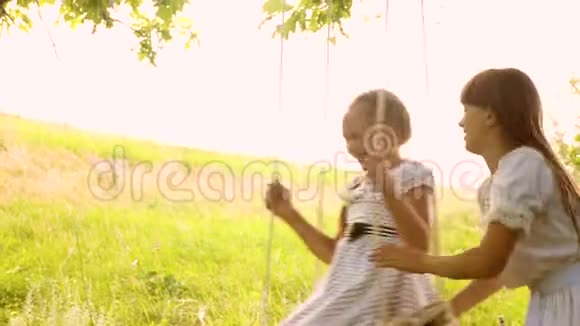 快乐的孩子们在公园的秋千上荡秋千姐妹们开心又笑慢动作视频的预览图