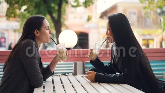美丽的年轻女士朋友们正在谈论一起坐在街头咖啡馆里喝着奶昔享受着饮料和饮料视频的预览图