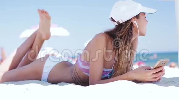 穿着比基尼头戴白色帽子的美丽放松苗条性感晒黑的女人躺在沙滩上白色的沙滩上白色的大个子视频的预览图