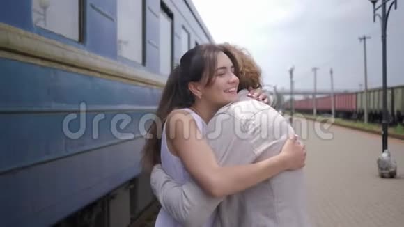 喜气洋洋的美女与男友拥抱分手后在火车站台上的货车旁欢笑视频的预览图