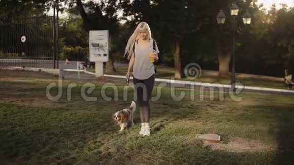 美丽的微笑着的金发女人和她的狗在公园散步她穿着休闲装视频的预览图