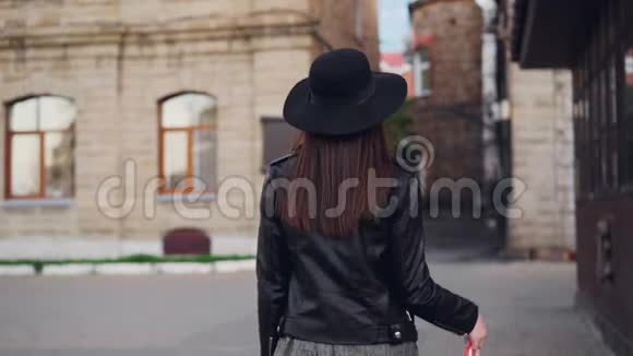 一幅美丽的黑发女郎带着购物袋走在街上然后转向镜头微笑的慢镜头肖像视频的预览图