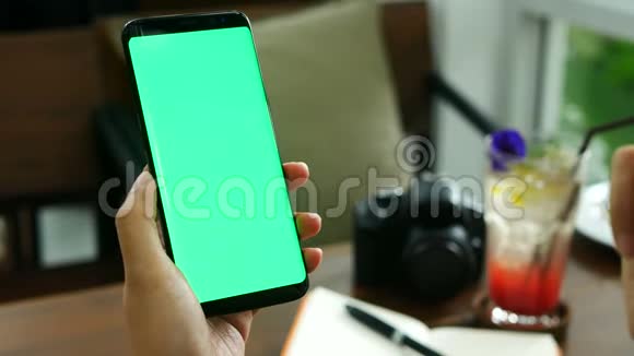 4K镜头在咖啡厅用绿色屏幕合上女人的手拿着智能的磨练滑动手指在手机屏幕上阅读视频的预览图