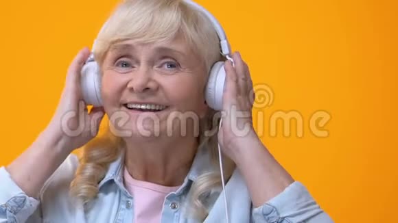 戴着白色耳机听音乐欣赏最喜爱的旋律的老年妇女视频的预览图