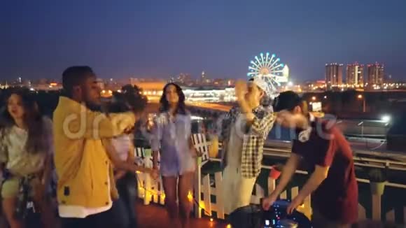 多种族的朋友们晚上在屋顶上跳舞开露天派对DJ则在使用设备视频的预览图