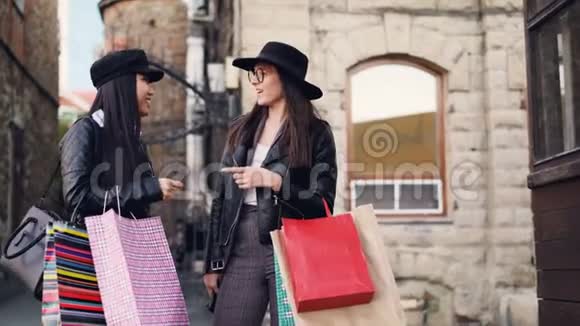 可爱的亚洲女孩正和她高加索的朋友说话她优雅的黑发女人站在街上拿着购物袋视频的预览图