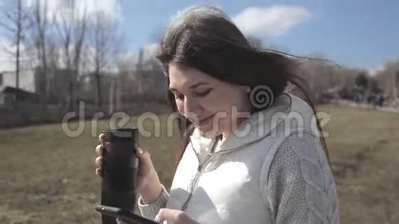 一个美丽的女孩走在公园里喝着热杯子里的咖啡在电话里发短信微笑着视频的预览图