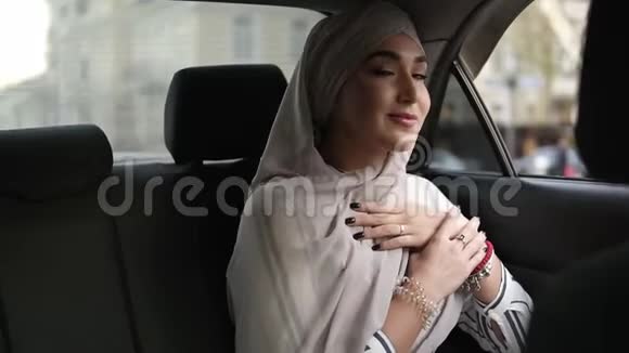 一位身穿米色头巾的年轻穆斯林妇女坐在车里从窗户往外看的画像视频的预览图