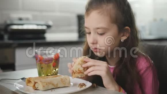 漂亮的小女孩在桌边吃煎饼和茶视频的预览图