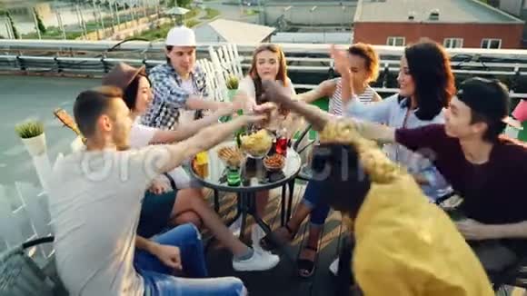 快乐的朋友们双手合十然后在空中高举围坐在屋顶的桌子旁喝酒视频的预览图