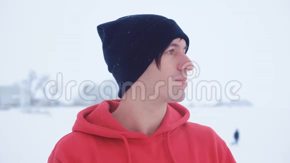黑帽年轻人的画像在冬季寒冷的户外雪地里微笑视频的预览图