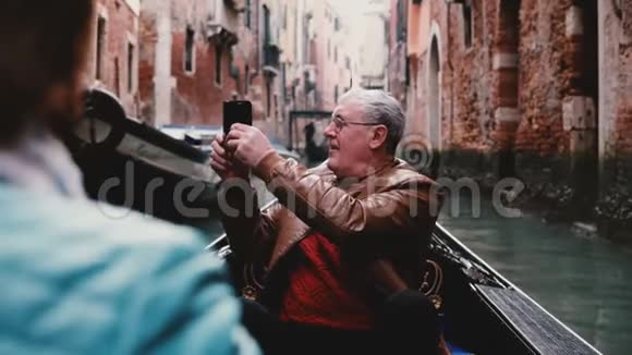 兴奋的欧洲资深男性游客在贡多拉微笑着环顾四周美丽的威尼斯运河之旅视频的预览图