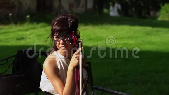 美丽的年轻女孩坐在长凳上在美丽的公园里拉小提琴视频的预览图