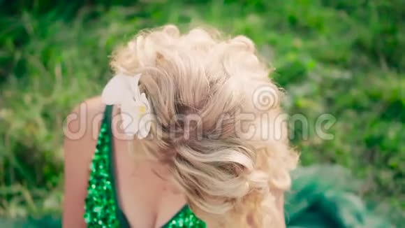 一位金发碧眼的白兰花的孕妇穿着一件绿绿色的长裙坐在草地上视频的预览图