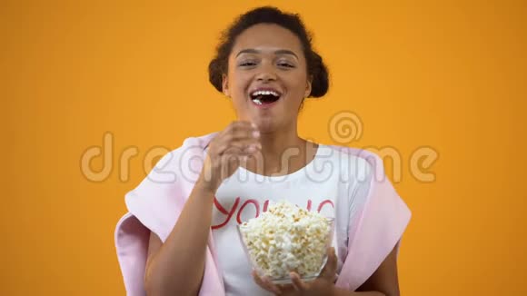 快乐的少女大笑享受电视上的喜剧片吃爆米花视频的预览图