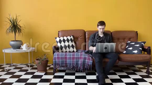在家里用笔记本电脑工作的年轻人库存录像盖伊在家工作坐在沙发上做笔记本电脑的自由职业者视频的预览图