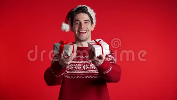 年轻的帅哥微笑着拿着礼品盒在红色的工作室背景上视频的预览图