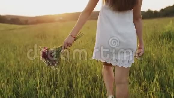 女人在乡间的田野里慢悠悠地走着手里拿着一束野花在草地上散步的女孩视频的预览图