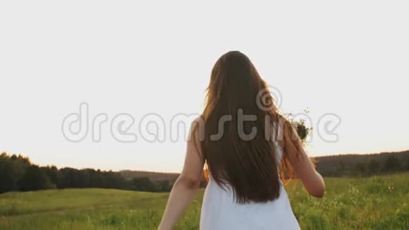 日落时分带着野花花束的女人在田野里奔跑在阳光照耀下的草地上享受自由视频的预览图