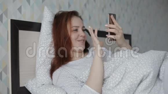 美丽开朗的女人躺在家里的床上用智能手机与朋友在线视频聊天视频的预览图