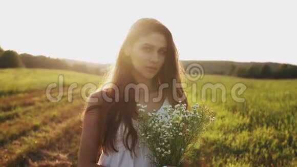 年轻女子站在草地上夏天的傍晚放着一束野花对着镜头微笑视频的预览图