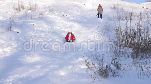 穿着红色夹克的小女孩在冬季公园里从雪山上滑下雪橇女孩欢笑着视频的预览图