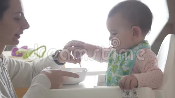 年轻快乐的妈妈教她蹒跚学步的孩子自己吃勺子婴儿食品视频的预览图