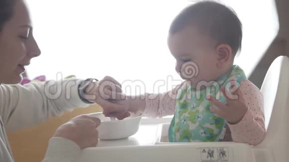 年轻快乐的妈妈教她蹒跚学步的孩子自己吃勺子婴儿食品视频的预览图