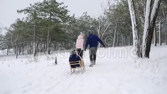 幸福的家庭在下雪的冬天滑雪父亲和母亲在下雪时带着儿子和女儿拉雪橇男孩和女孩视频的预览图
