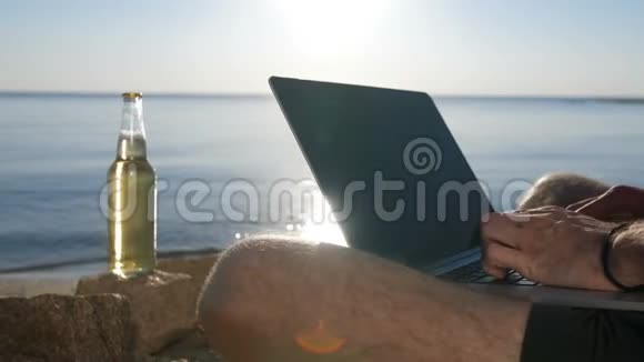 男性手在海滩上的现代笔记本电脑上打字视频的预览图