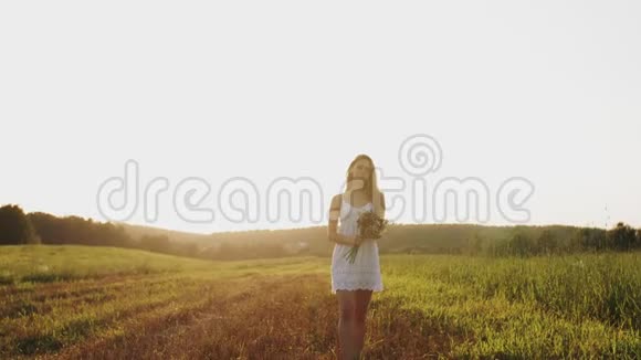 女孩站在田野里带着一束野花在太阳下绽放在夏夜的夕阳下阳光明媚视频的预览图