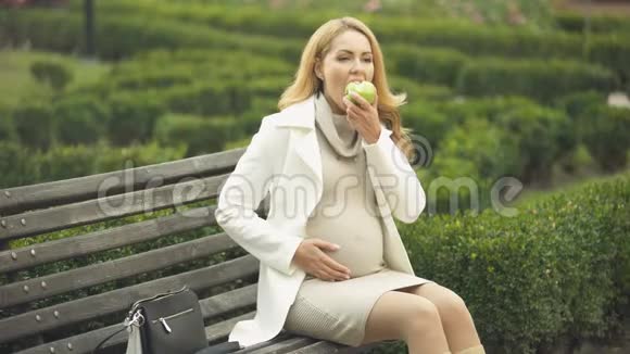漂亮的女人带着孩子吃绿苹果坐在公园的长凳上维生素视频的预览图