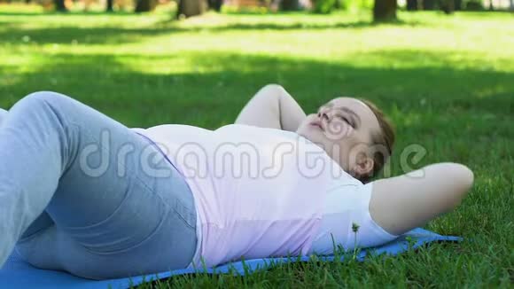 胖女孩几乎不做俯卧撑躺在公园的垫子上精疲力竭的锻炼节食视频的预览图