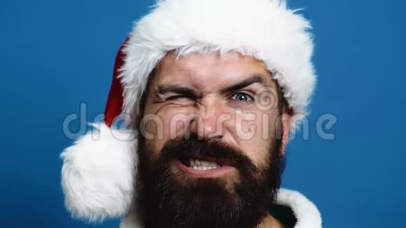 戴着新年帽子胡子男在蓝色背景上做鬼脸蓝色背景的搞笑圣诞老人概念视频的预览图