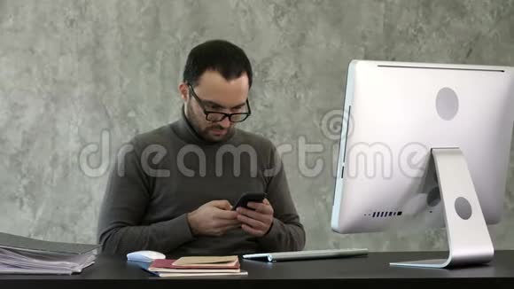 留胡子的年轻商人在现代办公室工作男人看着他的智能手机打字视频的预览图