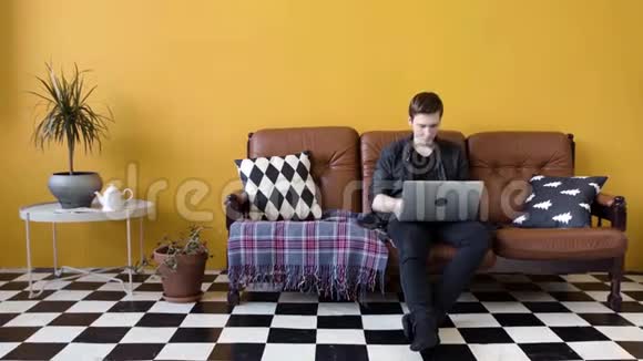 在家里用笔记本电脑工作的年轻人库存录像盖伊在家工作坐在沙发上做笔记本电脑的自由职业者视频的预览图