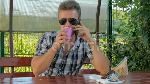 戴眼镜的男人在露台上打电话吃咖啡三明治视频的预览图