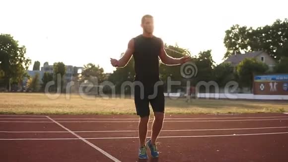 白人运动员穿着黑色运动服在体育场的跑道上跳过跳绳太阳照耀着视频的预览图