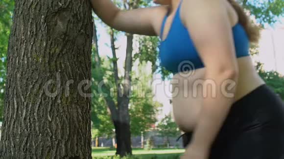 胖女人喘着粗气站在树下做运动减肥视频的预览图